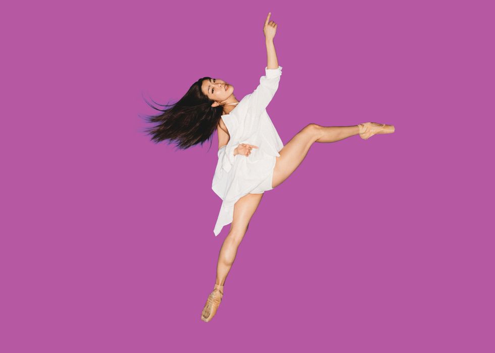 Andrea Yorita balances in an off-kilter attitude front en pointe, white blouse and dark hair swaying with the motion. Her working arm extends delicately before her as she gazes back toward the camera.