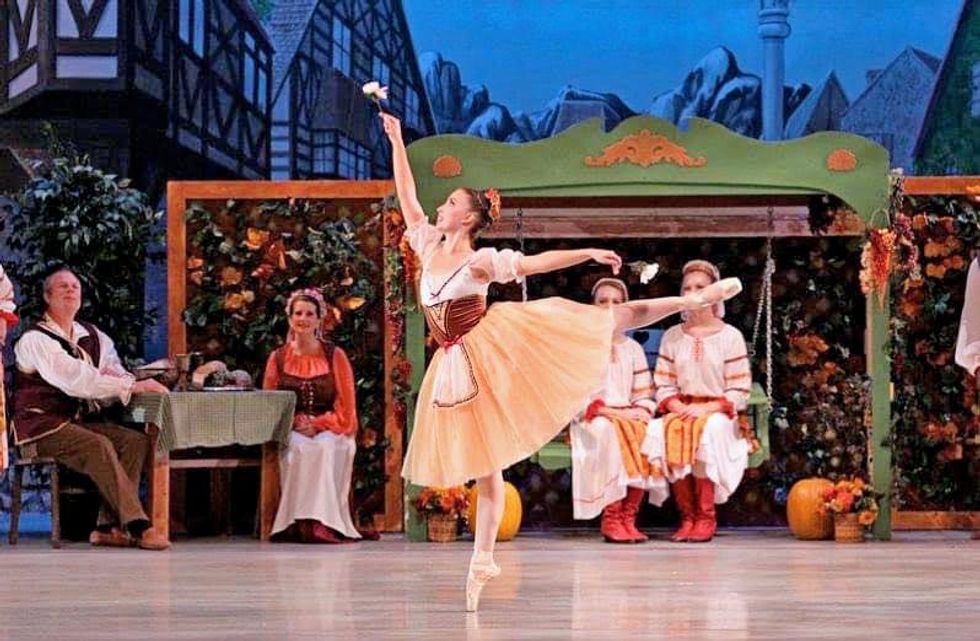 Brigid Polei stands on pointe in arabesque wearing a peasant dress with a romantic tutu.