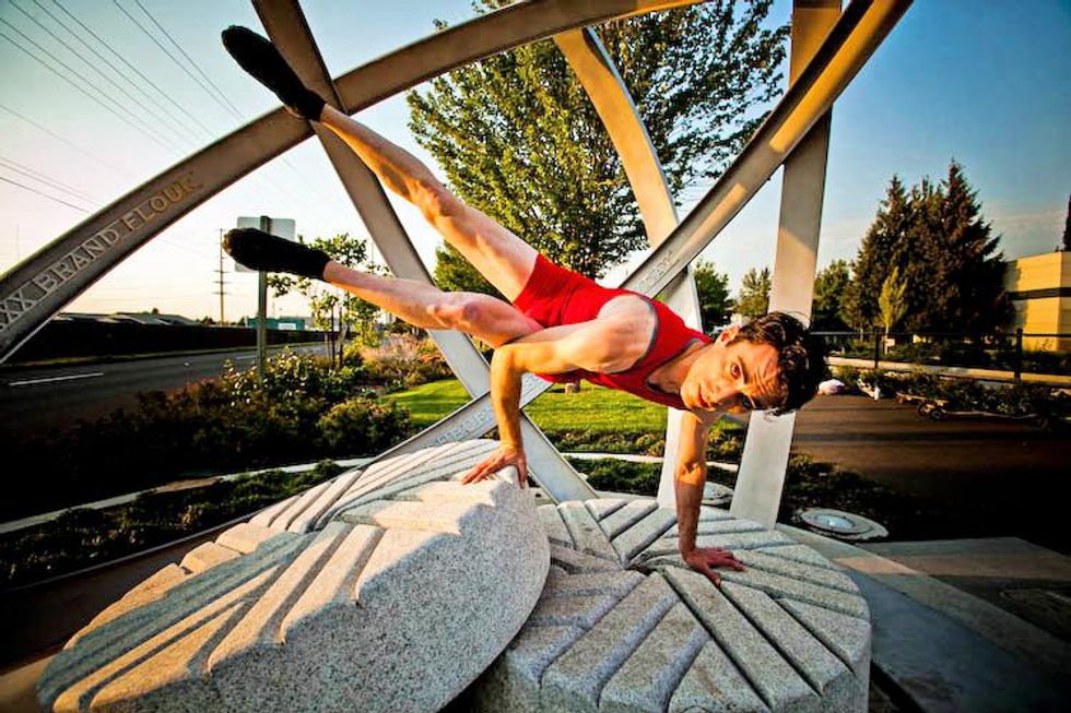 Benjamin Goodly balances on his hands with his body in the air on a concrete sculpture structure outdoors.