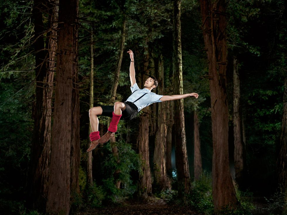 Garen Scribner, in short sleeves, red legwarmers, and suspenders, falls serenely through the air, back nearly parallel to the ground, against a backdrop of a spooky forest.