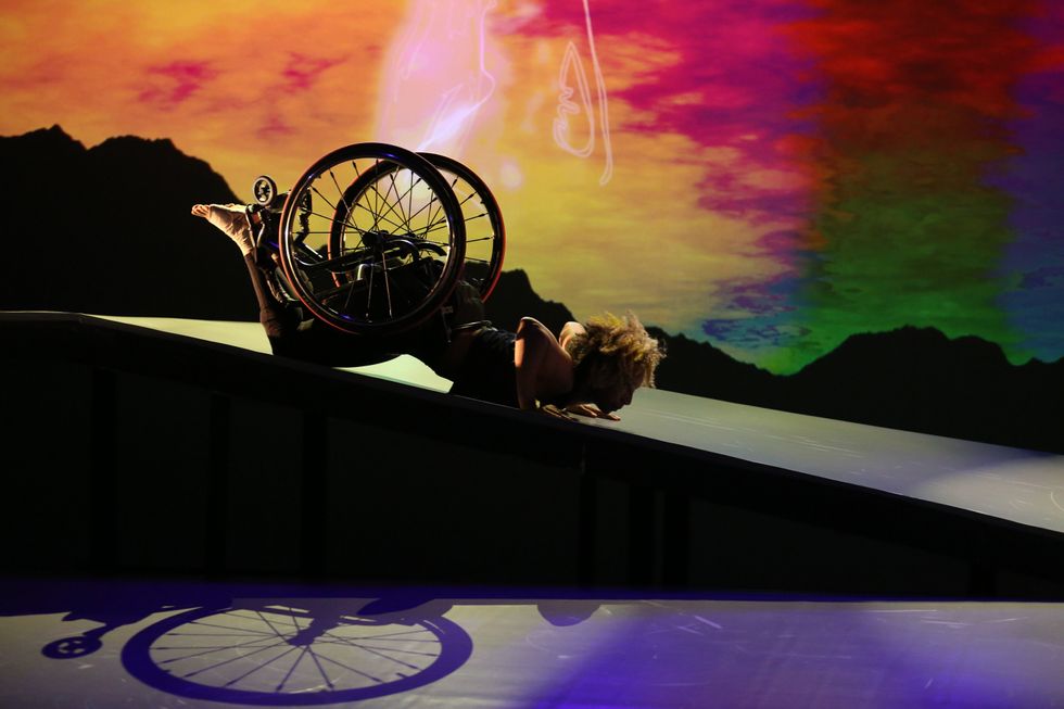 Alice Sheppard on the ramp for DESCENT. She is face down, supporting her weight with her hands. A shadow of her chair is illuminated by the stage lighting. Photo courtesy MANCC. 