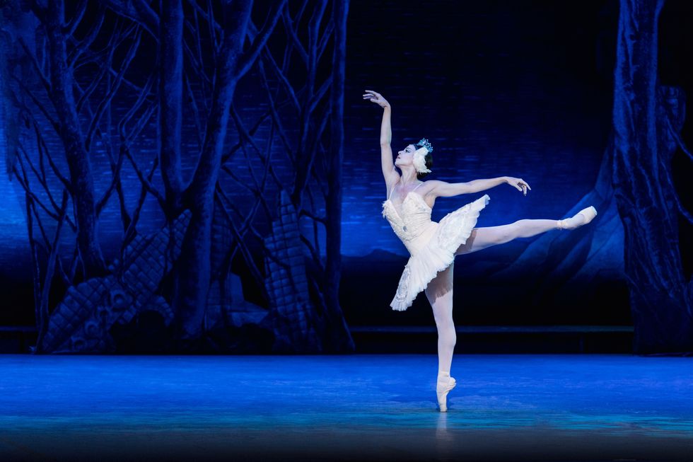 Valdu00e9s, in the white tutu and headpiece typical for Swan Lake's white acts, balances in first arabesque on pointe.