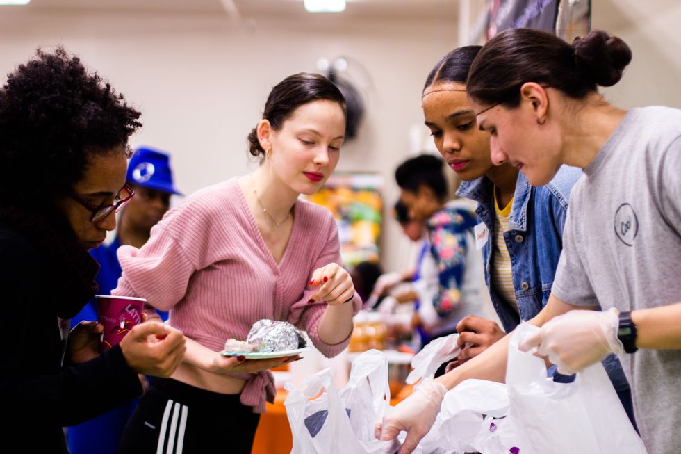 Four young women stand over bags of groceries, chatting