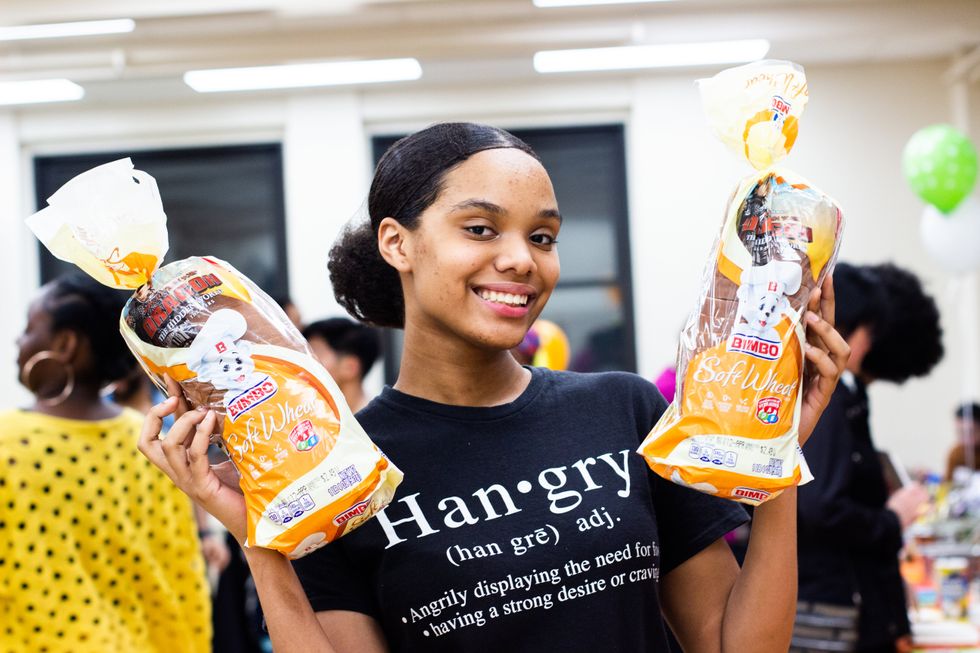 A young woman smiles and holds up two loaves of bread. Her shirt says "hangry"