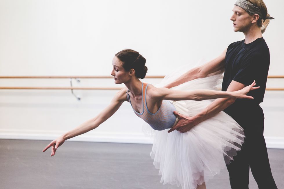 David Hallberg partners Amber Scott as she leans forward in an arabesque in a rehearsal tutu.
