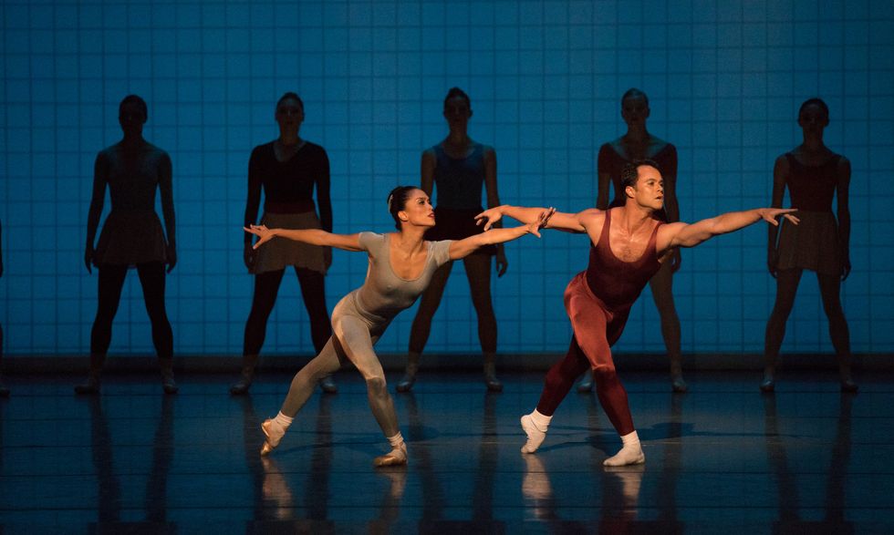 Cirio (in a gray unitard) and Arrais (in a red unitard) are both in deep lunges. Five dancers stand, facing front, in the background. 