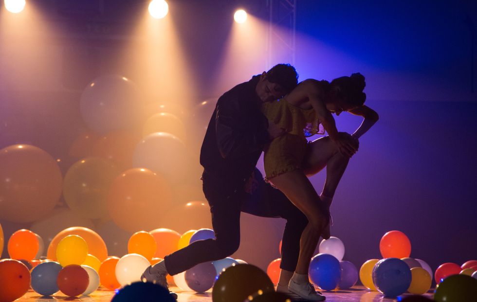 Two dancers embracing in an empty gym full of balloons.