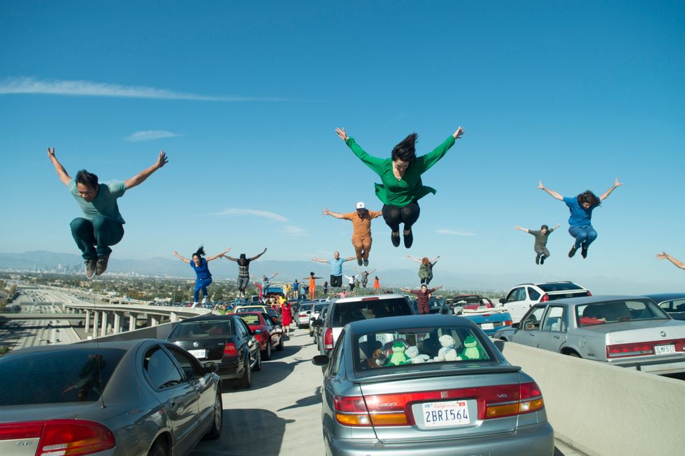 A busy LA highway, with dancers middair jumping on top of the cars.