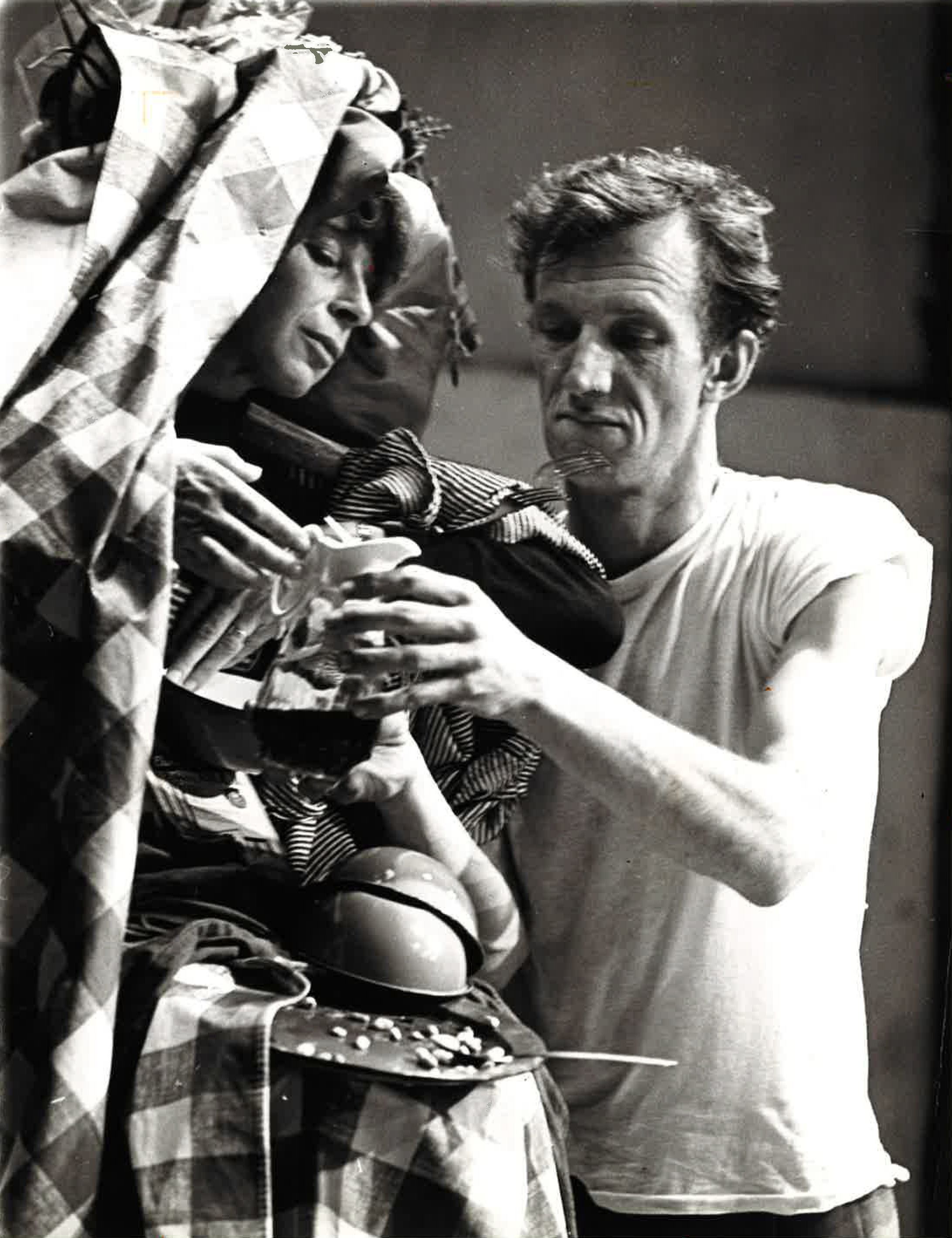 Anna Halprin seems serene as John Graham, in a simple white t-shirt, passes her a pitcher of dark liquid. Halprin is swaddled in a checkered blanket, and is already improbably balancing dirty plates, bowls, and utensils.