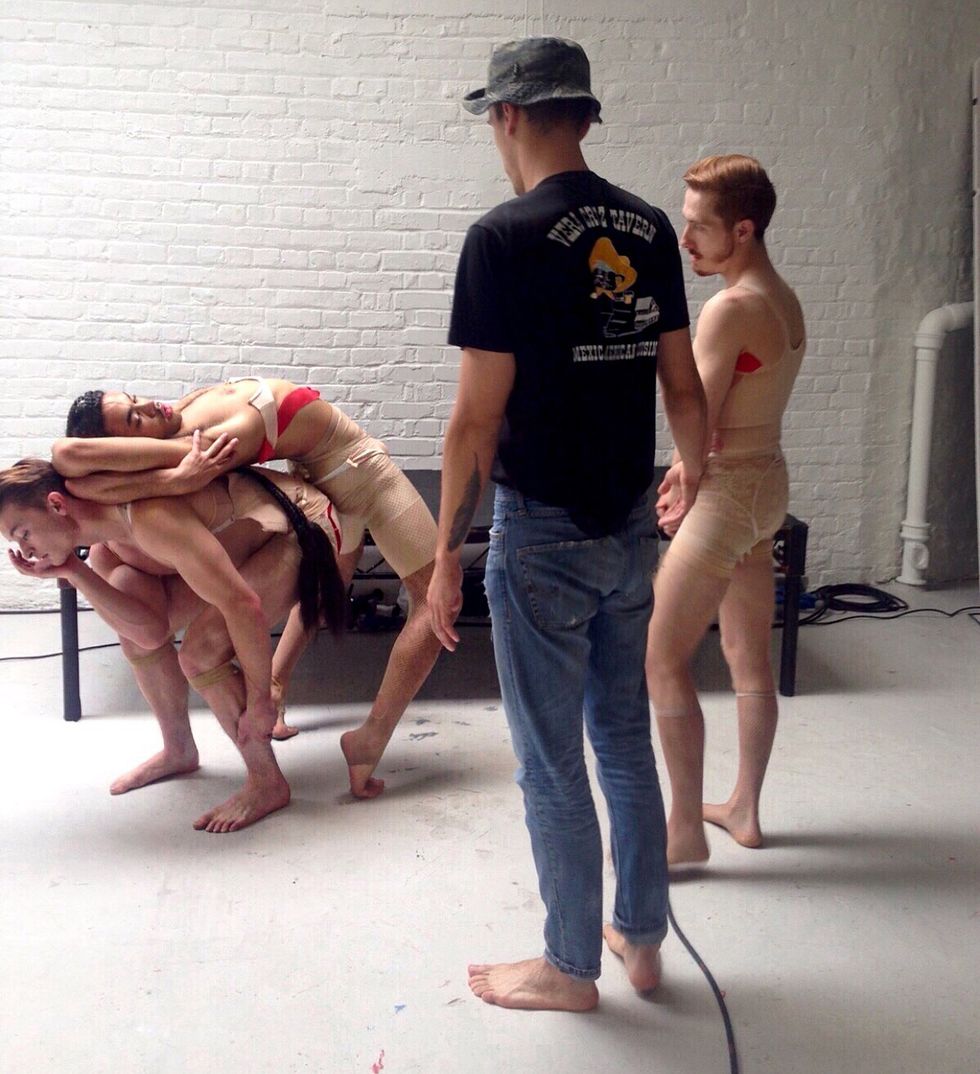Boguslawski oversees a group of models in nude and red clothing hunched over each other