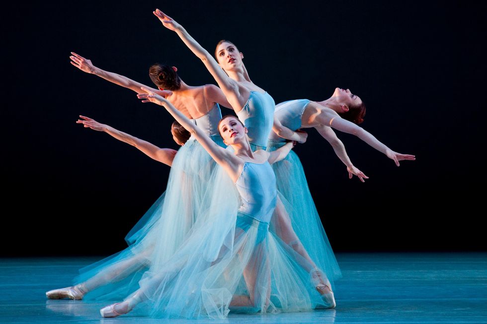 Emily Adams and four other women in light blue leotards and matching long tulle skirts link together, each extending one arm on the diagonal on different levels