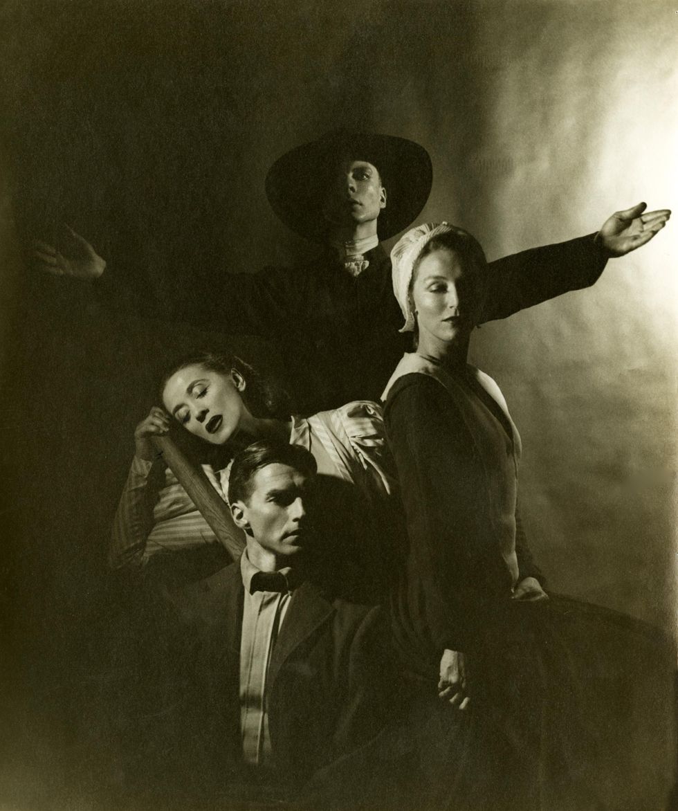 An archival shot of the cast of Appalachian Spring photographed in the manner of an older family portrait. The preacher stands behind, arms outstretched; the two pioneer women gaze demurely down, and the besuited pioneer man looks seriously into the distance.