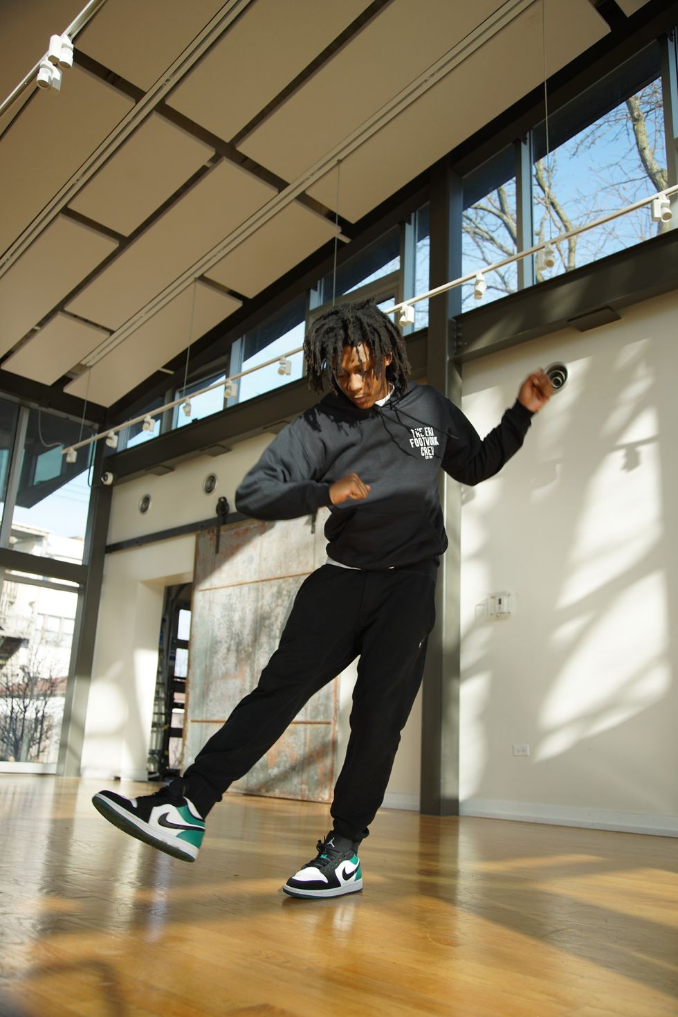 Sterling "Steelo" Lofton, a Black man with chin-length dreadlocks, tilts off center on one leg, watching his extended leg as it begins to cross center.