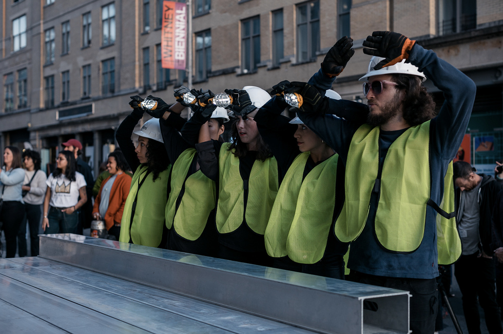 A line of people in construction helmets and green vests adjust their headlamps.