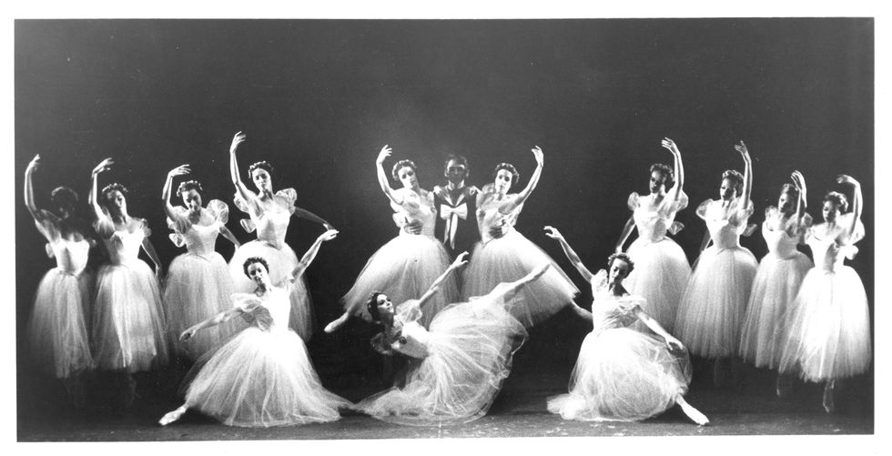 Thirteen ballerinas in white Romantic tutus and one danseur in a dark tunic create a tableau onstage.