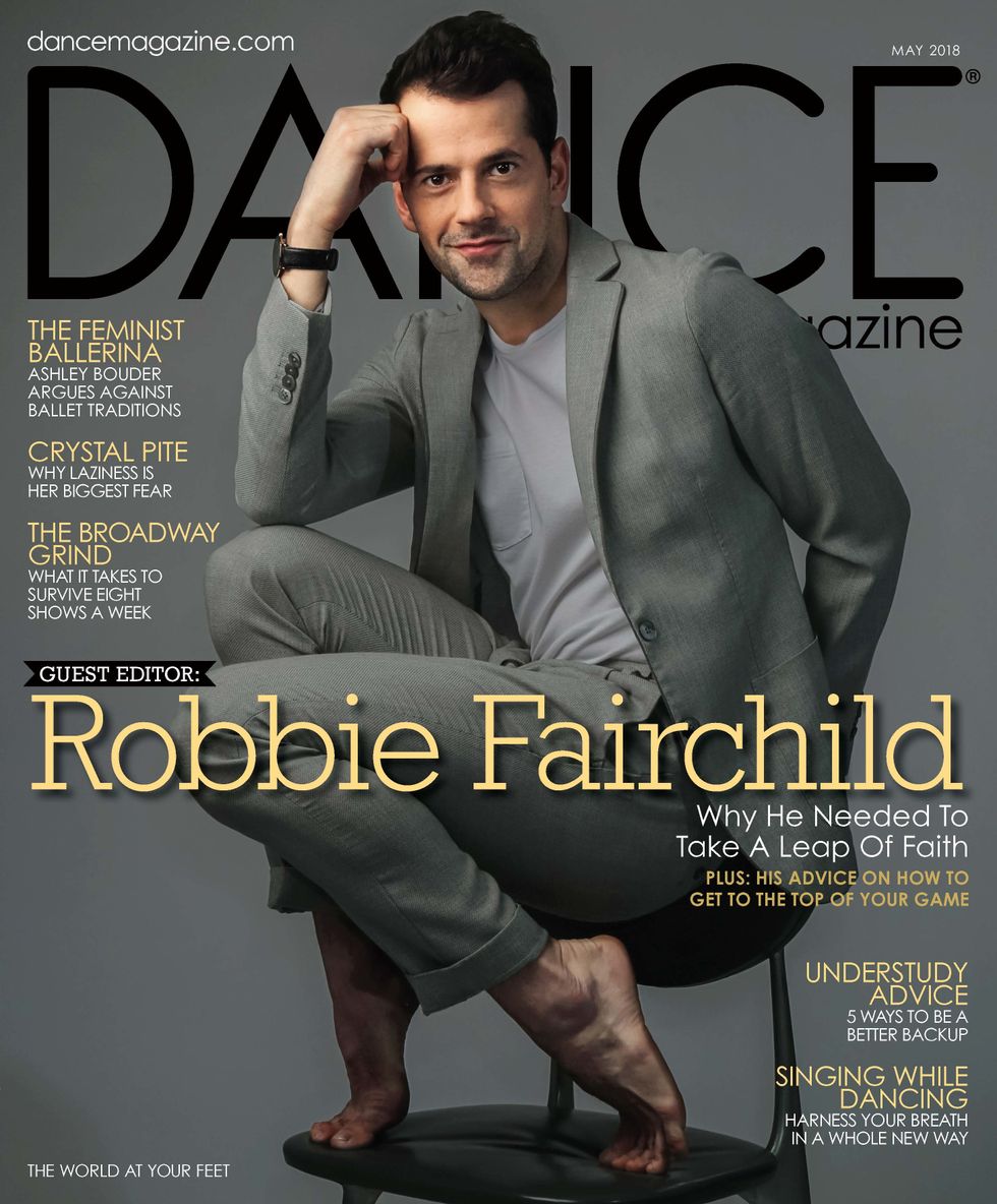 Robbie Fairchild on Dance Magazine's May issue crouches on a chair in a gray suit
