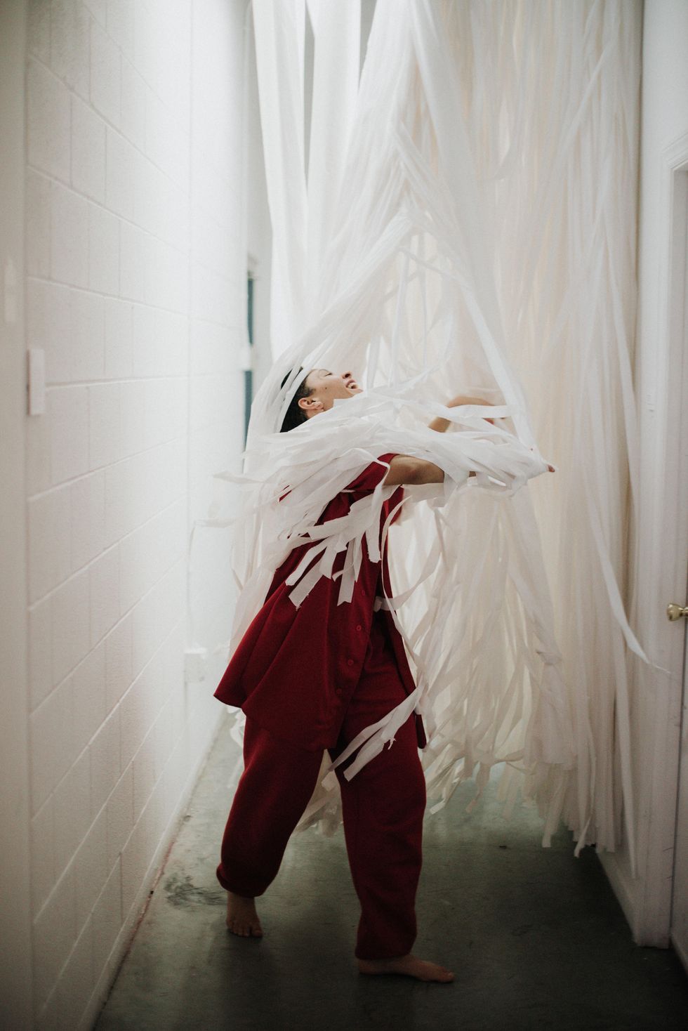 Myssi Robinson joyfully dances through a curtain of white streamers, her head thrown back as she smiles widely. Her arms slice through the streamers.