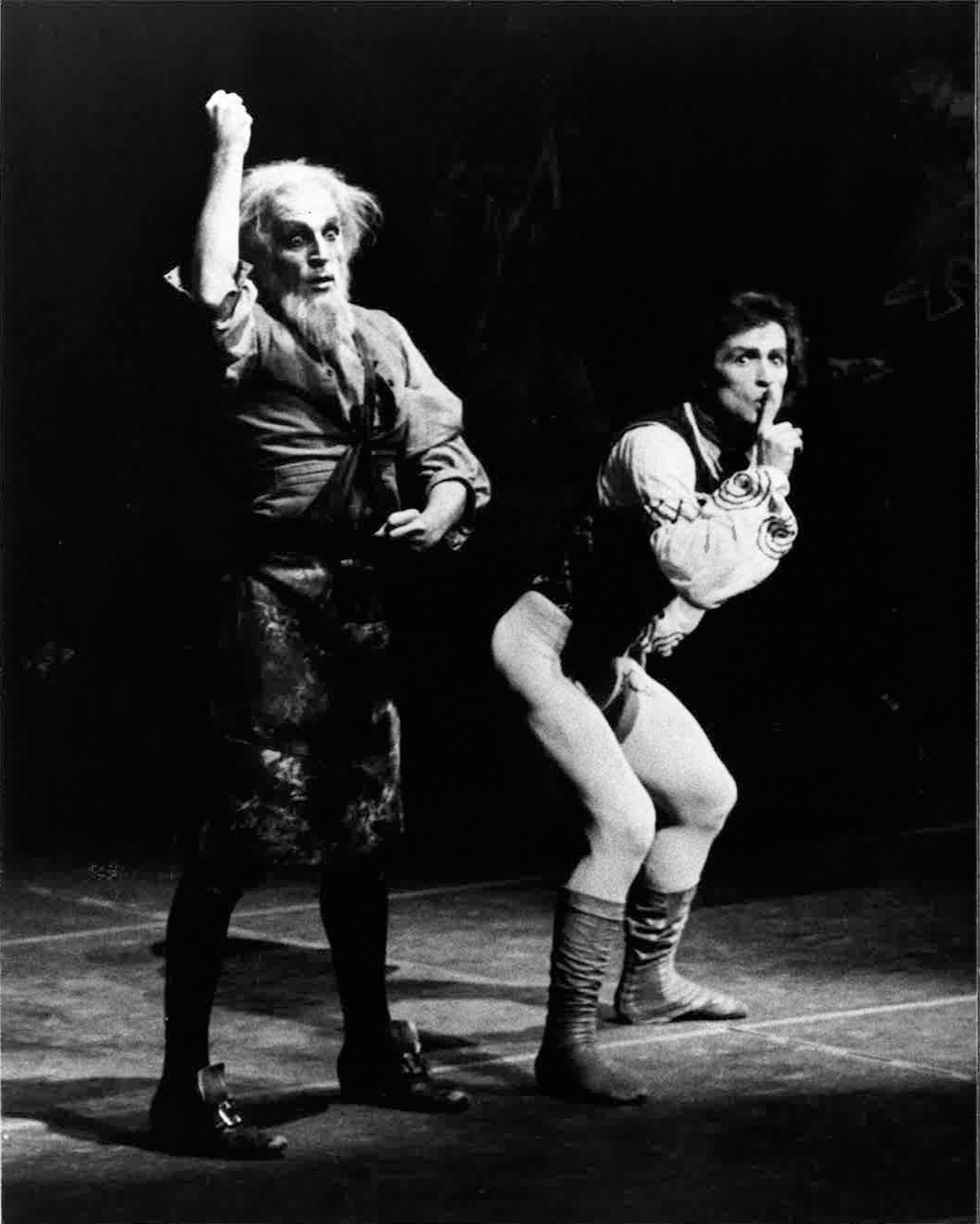 Rudolf Nureyev doubles over, holding a finger to his lips with a concerned look, as Erik Bruhn, barely recognizable under a shock of white hair and a riotous beard, pauses, wide-eyed and unseeing, right next to him.
