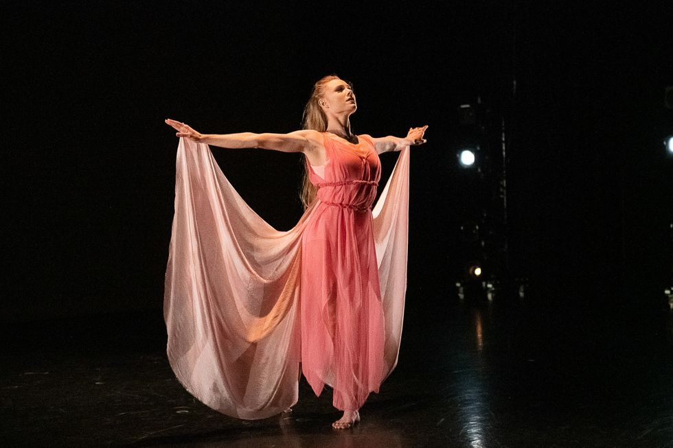 Sara Mearns in a pink dress and fabric that looks like wings, her arms spread wide