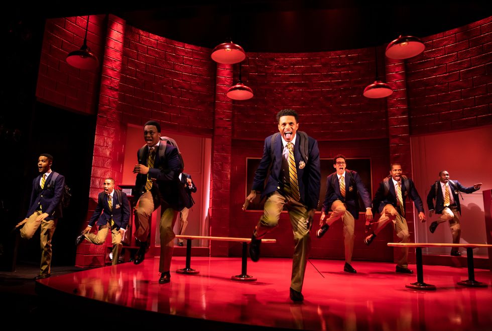 An image from Choir Boy, featuring male students stepping enthusiastically in school uniforms of khaki pants, dress shoes, gold ties and navy blazers.