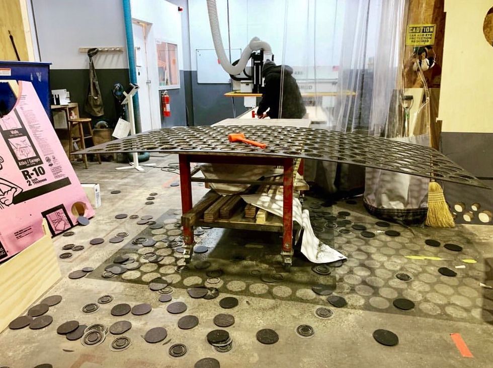 A cluttered theater set-building workshop featuring a cart with a piece of stage floor. Circles have been punched out of the floor material.