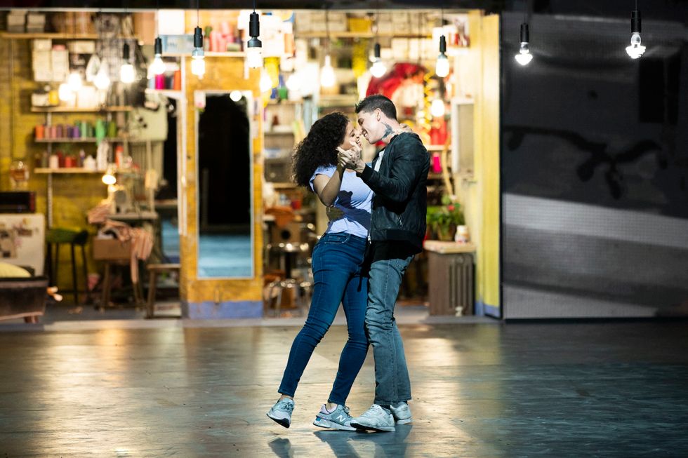 Two dancers in jeans and sneakers sway, holding each other in their arms