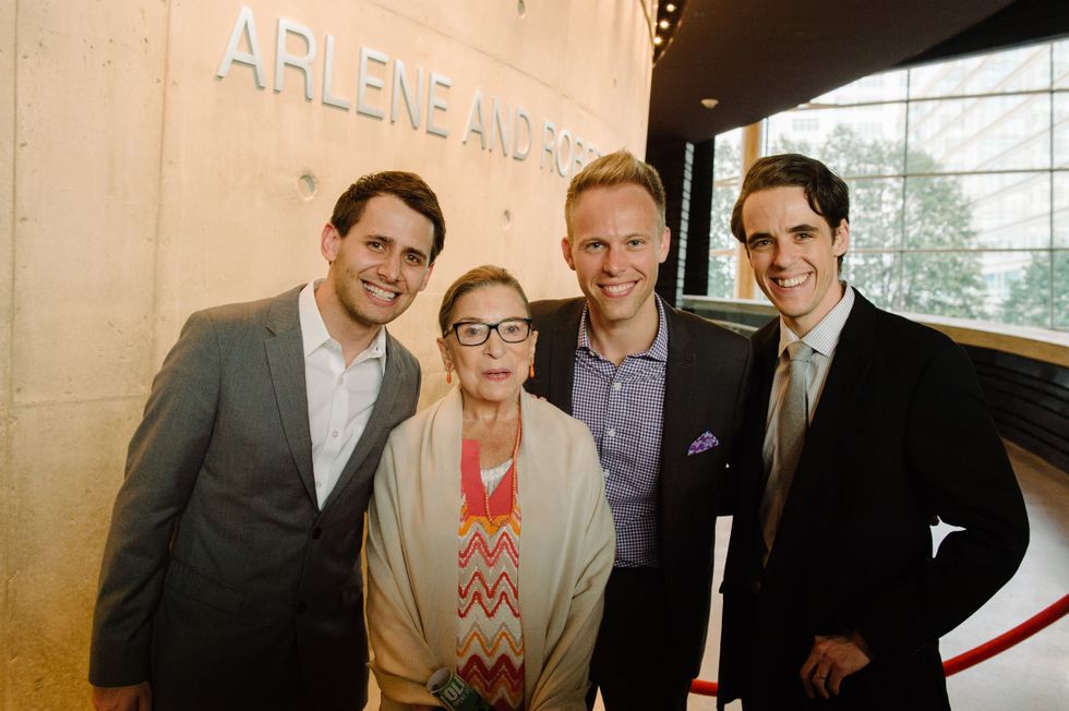 Three grinning young men stand around Ruth Bader Ginsburg in the atrium of Arena Stage.