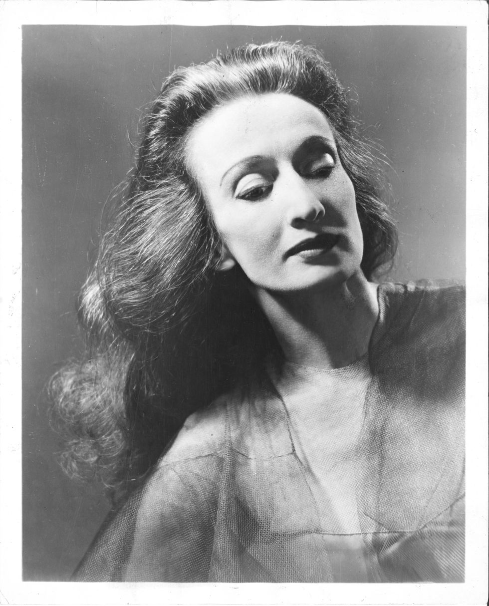A black and white headshot of Doris Humphrey, coifed hair waving past her shoulders, angular features caught in a moment of repose.