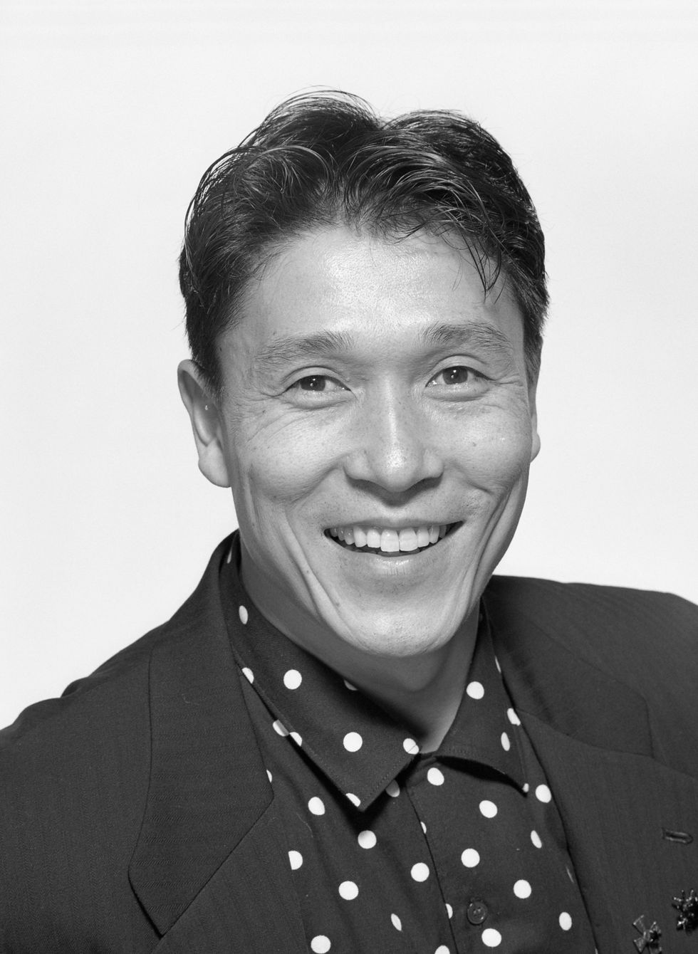 A black-and-white headshot of Masazumi Chaya. He is an Asian man and is wearing a suit jacket and polka dot dress shirt.