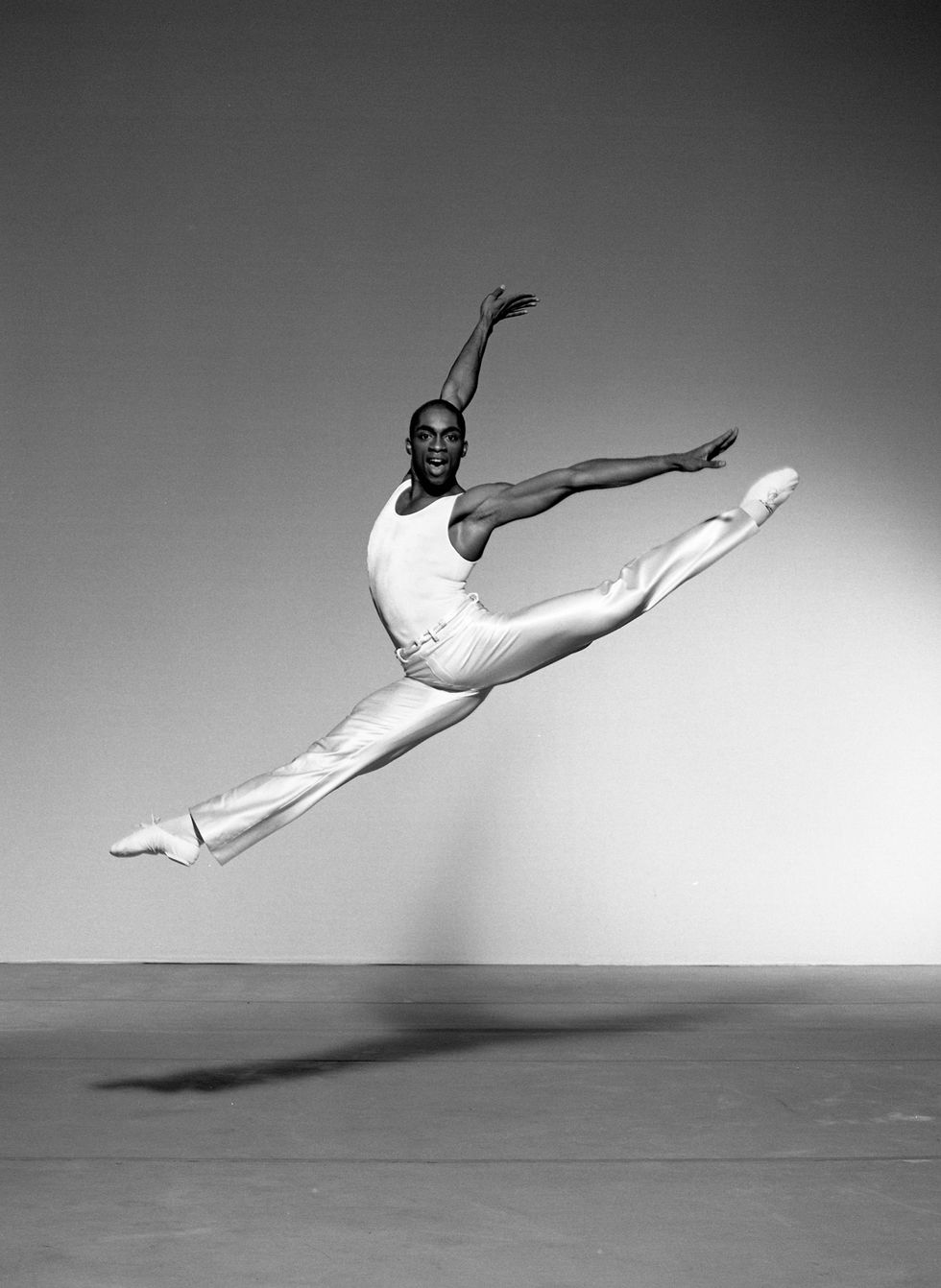 A black-and-white image of a tall, black man doing a split leap