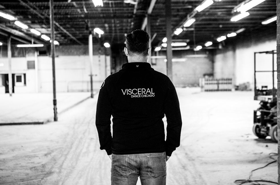 Nick Pupillo stands with his back to the camera, wearing a sweatshirt that reads "Visceral Dance Chicago." In the background, a large, warehouse-like space that will become a studio is under construction.