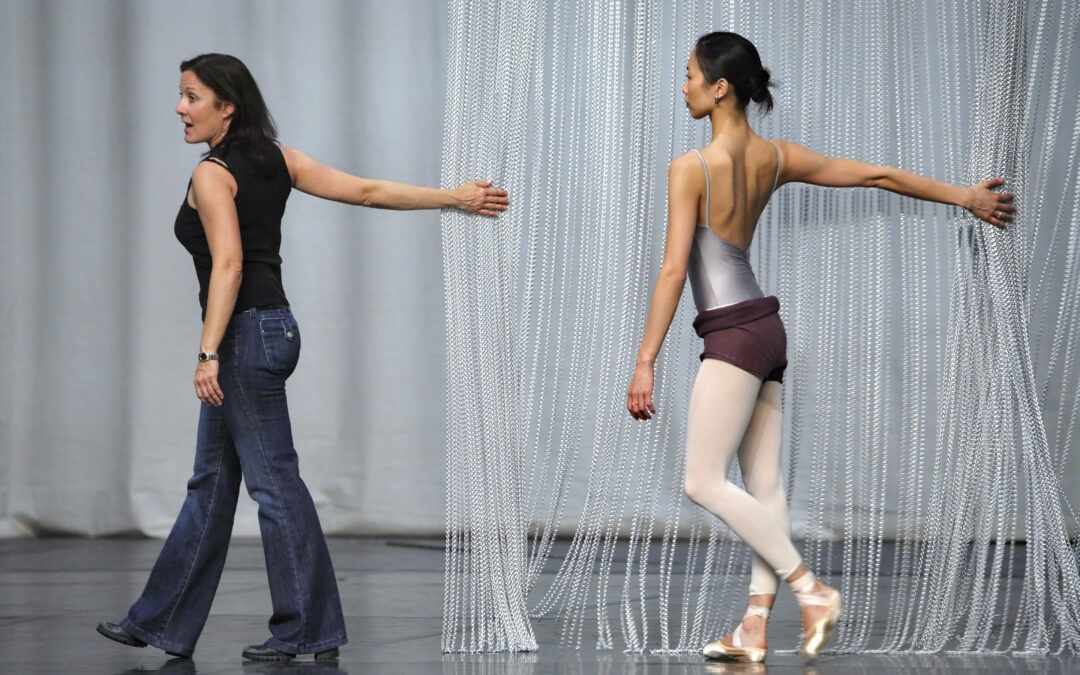 a female choreographer wearing jeans and a black tank top teaching a dancer in a studio