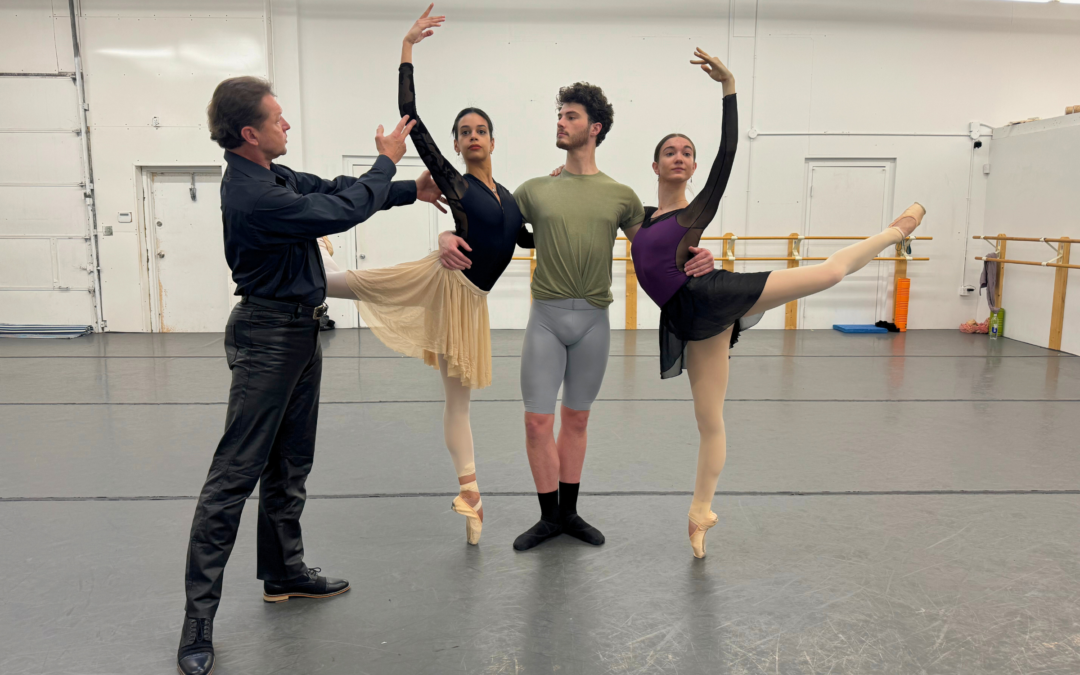 In a dance studio, Timour Bourtasenkov directs a trio of dancers. Gabriela Checo and Breanna Faith Justus pose on either side of Covington Pearson, who supports them as they stand on pointe in attitude derriere.