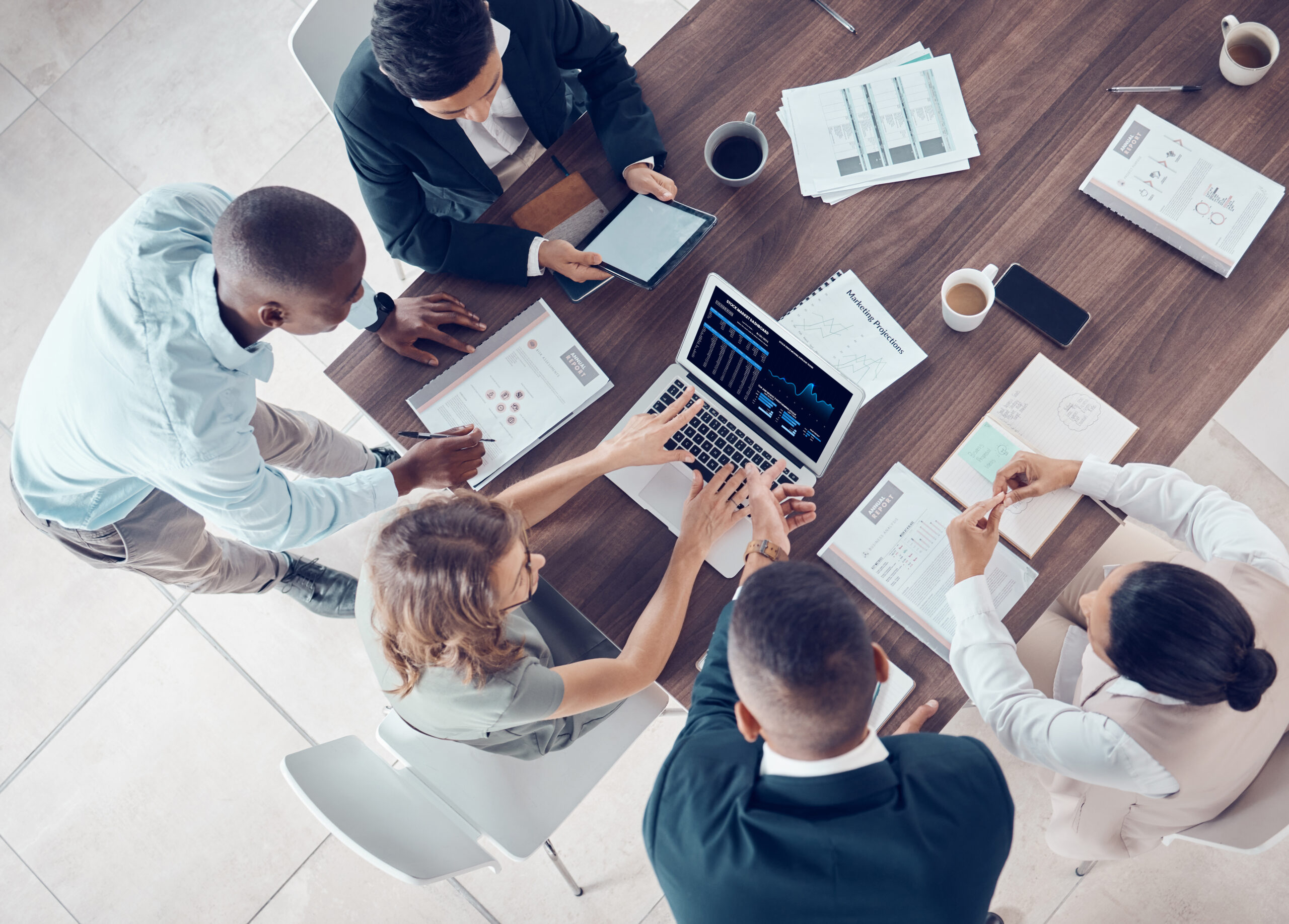 a group of people sitting around a table with laptops and notebooks