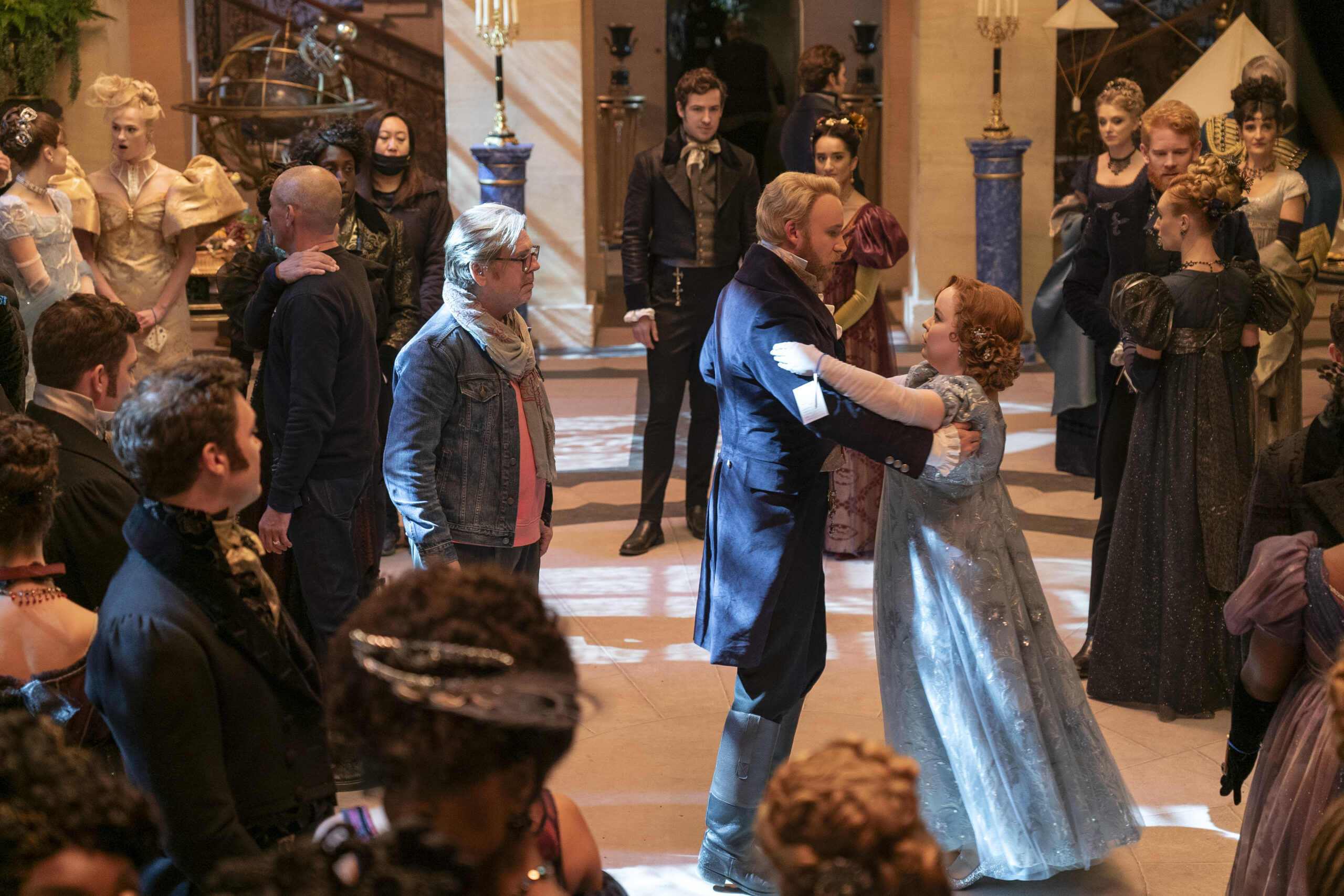 a male choreographer watching a couple dance in a ballroom