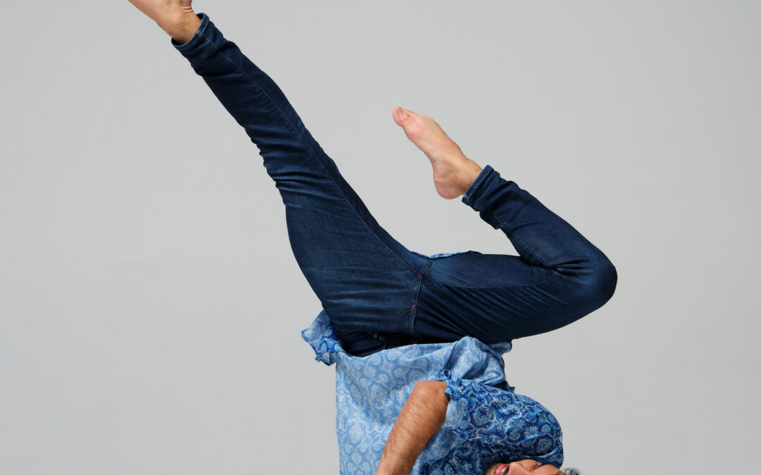 a male dancer performing a shoulder stand against a white backdrop