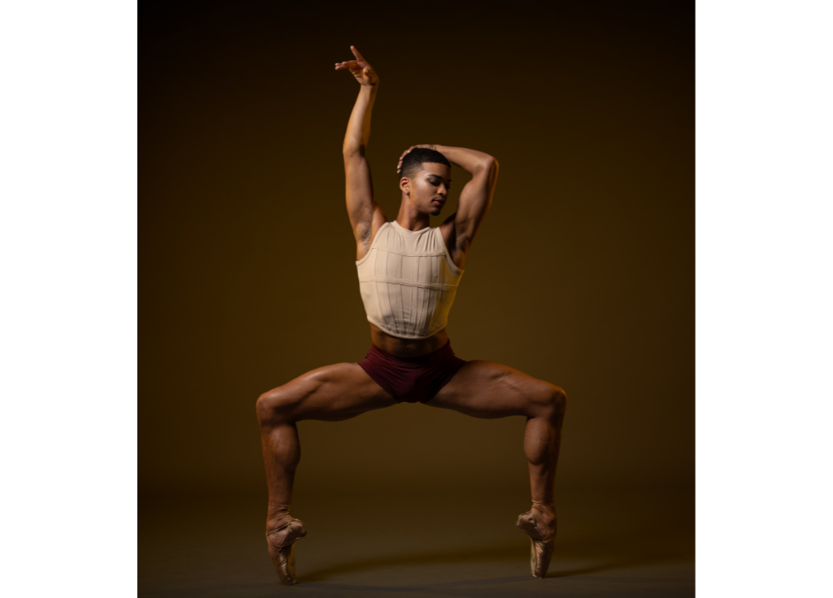 a male dancer on pointe posing in a wide second with one arm up