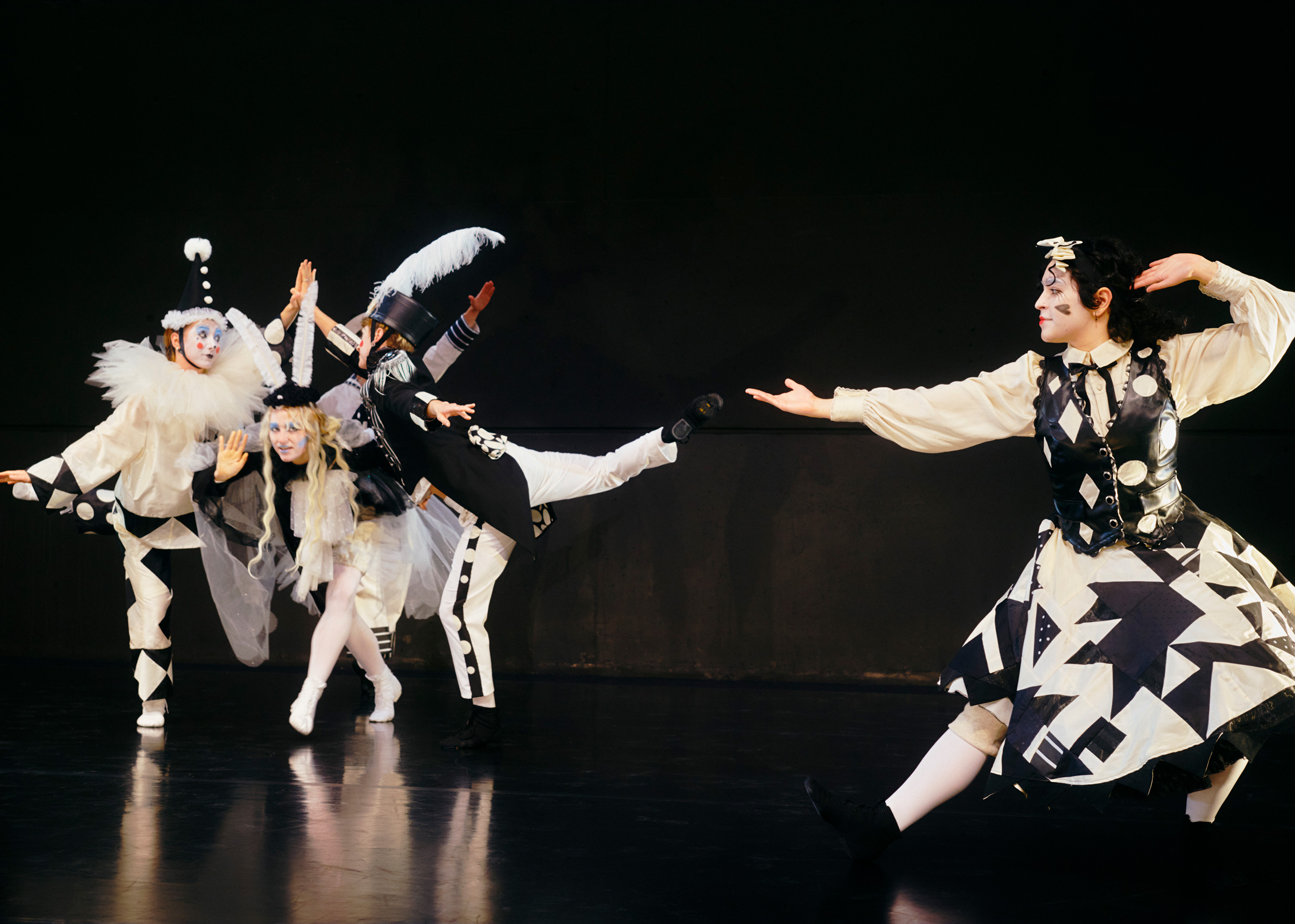 Four dancers in graphic black-and-white costumes and makeup perform in front of a black backdrop.