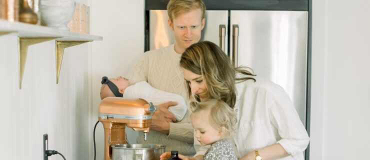 A man holding a baby, a woman and a child hulge over a kitchen mixer