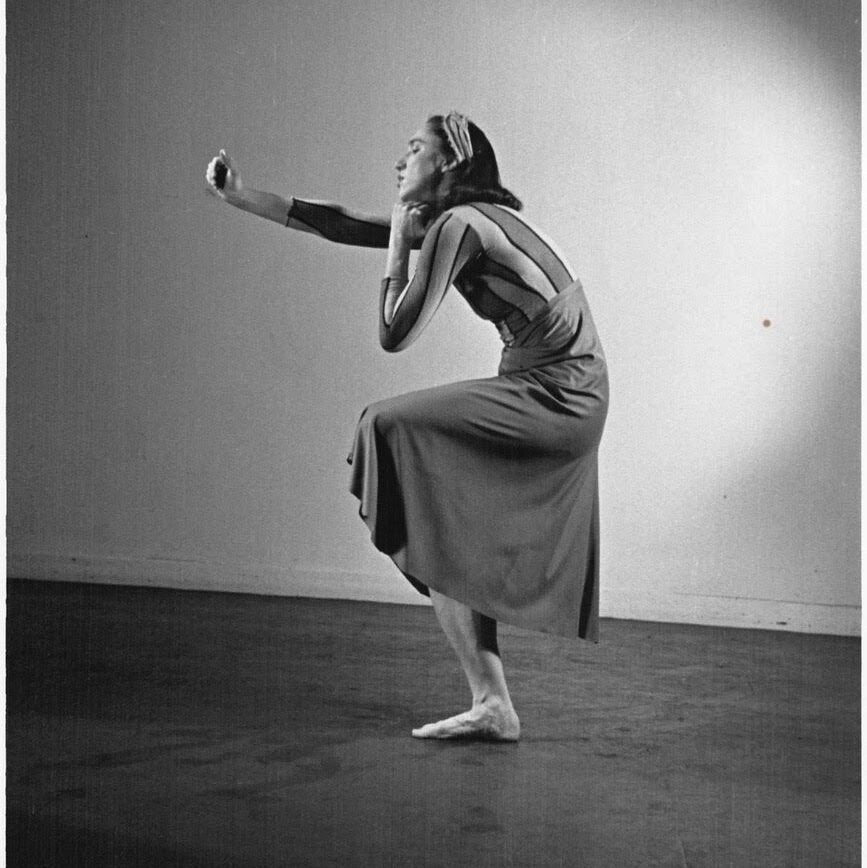 a female dancer contacting in a parallel passe with one arm outstretched 