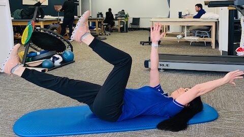 a female physical therapist demonstrating by extending one arm overhead and the opposite leg out