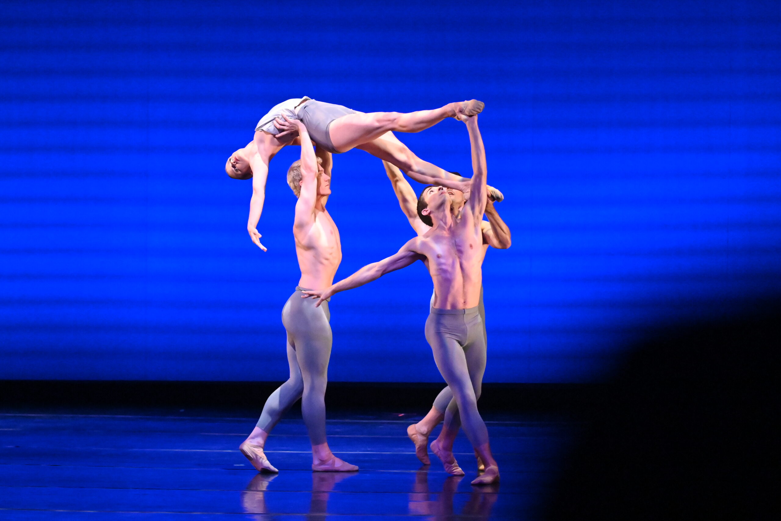 three male dancers lifting a female dancer over their head on stage