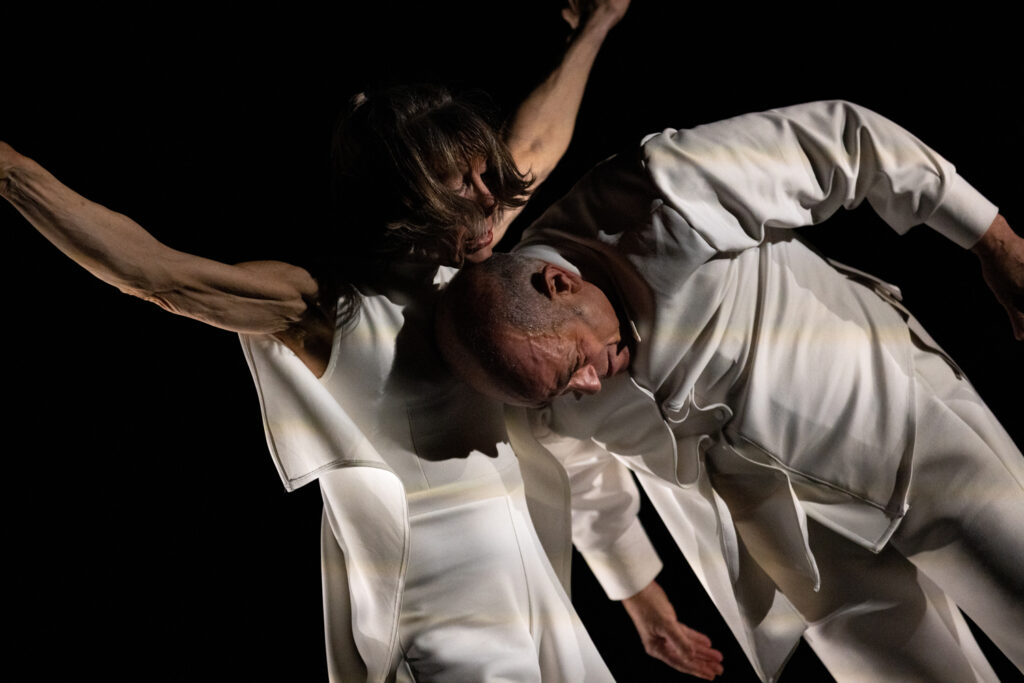 In a close-cropped image, Dorfman uses the back of his head to support Race, who has her arms raised angelically, under her chin. Both wear white tailored costumes.