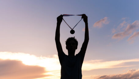 Silhouette of an athlete celebrating the gold medal against a sunset sky adorned with golden clouds in the background.