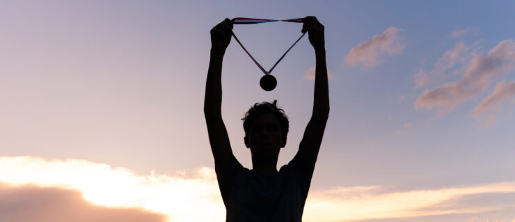 Silhouette of an athlete celebrating the gold medal against a sunset sky adorned with golden clouds in the background.