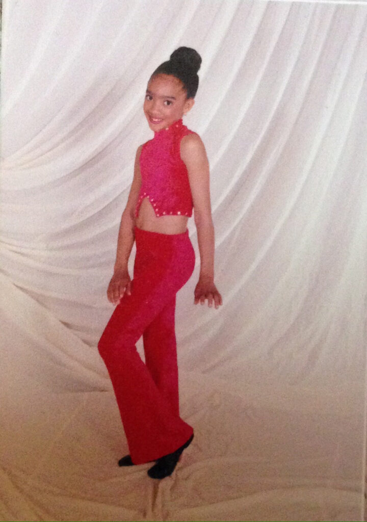 a young dancer wearing bright red pants and top posing against a white backdrop 