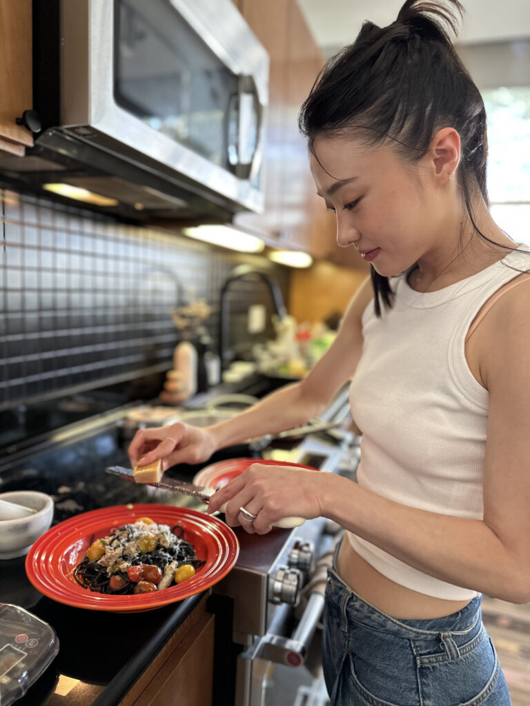 a woman standing in the kitchen preparing a bowl full of food