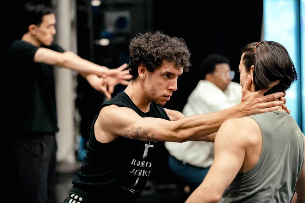 Two dancers face each other, one clasping the other's neck with both hands with an intense glare.