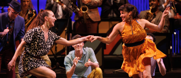 two female dancers swing dancing in the center with an audience watching on