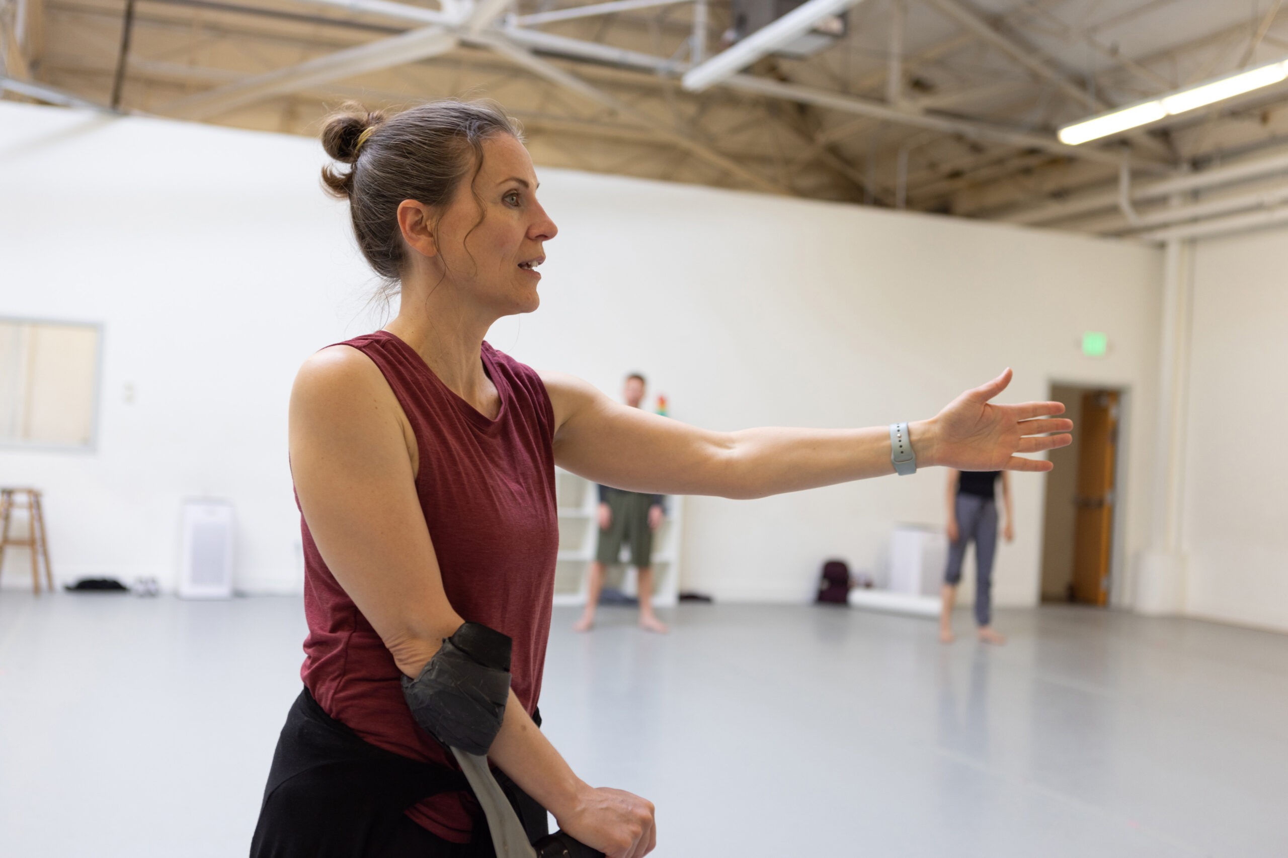 Nadia Adame rehearses in the studio. She is a light-skinned Hispanic woman with brown hair in a ponytail; she is a cane user and wears a maroon tank top.